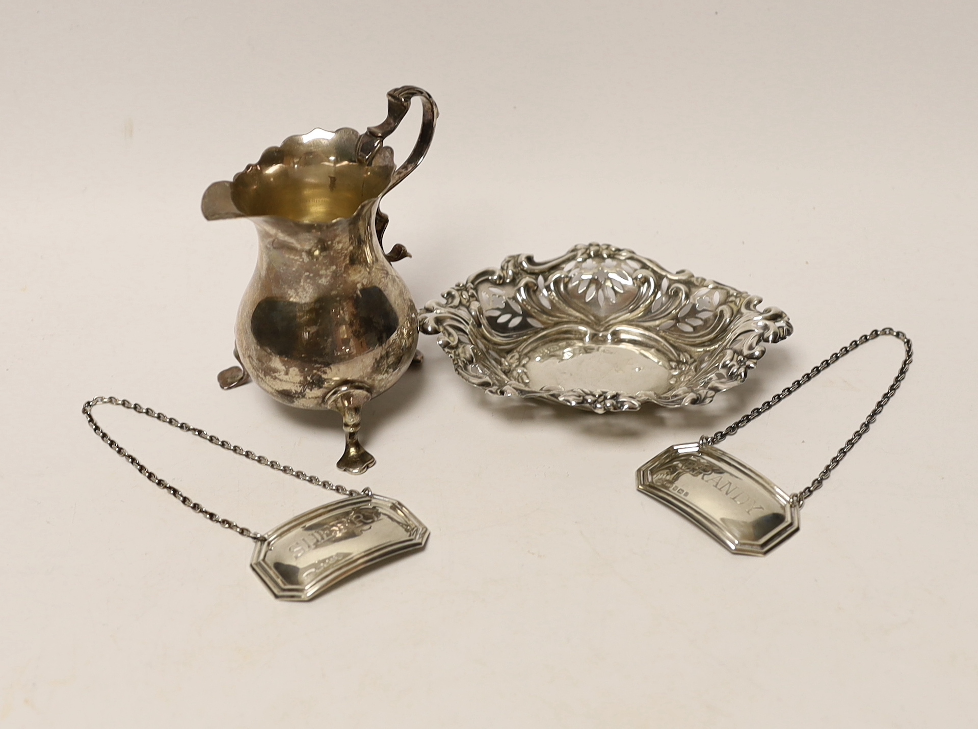 A late Victorian silver cream jug, Birmingham, 1894, 93mm, a repousse silver bonbon dish and a pair of modern silver wine labels.